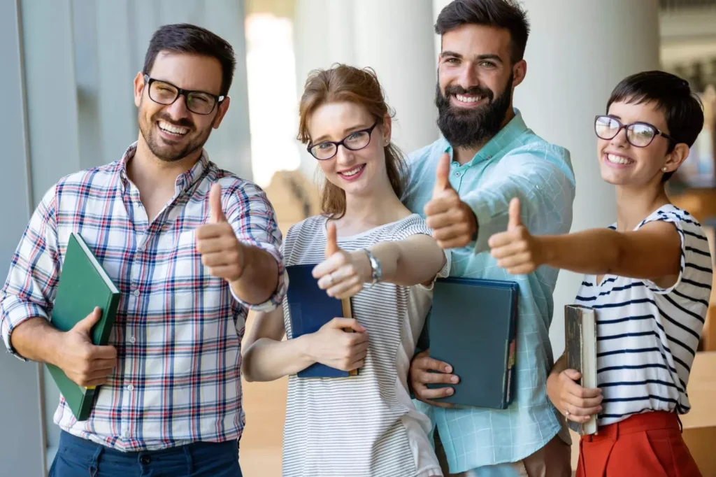 Group of students holding books and giving thumbs up
