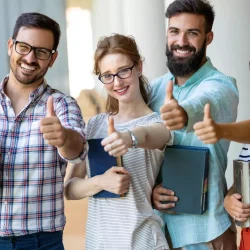 Group of students holding books and giving thumbs up